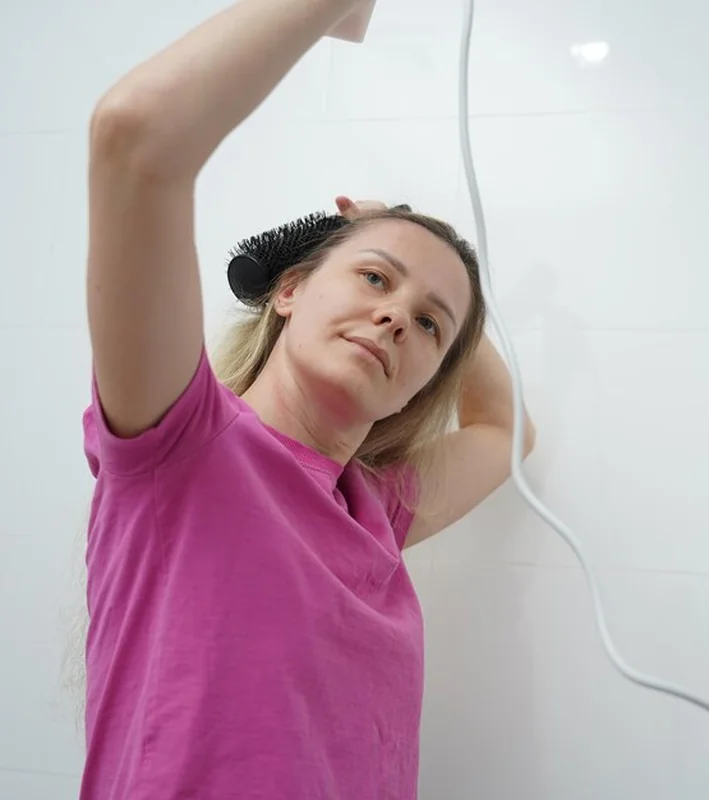 Kobieta suszy i czesze włosy w łazience