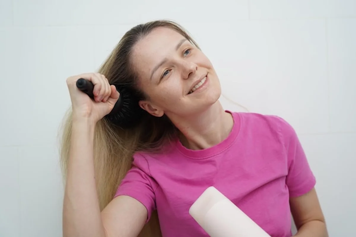 Kobieta suszy i układa włosy w łazience za pomocą suszarki i szczotki