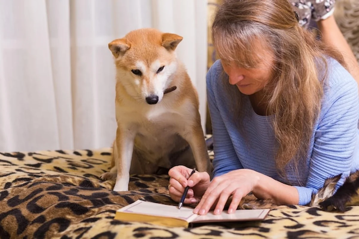 Kobieta pisząca w pamiętniku z psem rasy shiba inu na łóżku